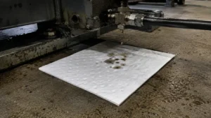 White oil-only absorbent pad positioned under a dripping hydraulic fitting on an industrial machine, catching oil drops.